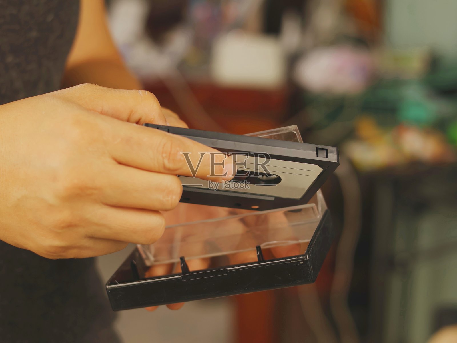 一双手将一盘老式录音磁带放入透明塑料盒中照片摄影图片