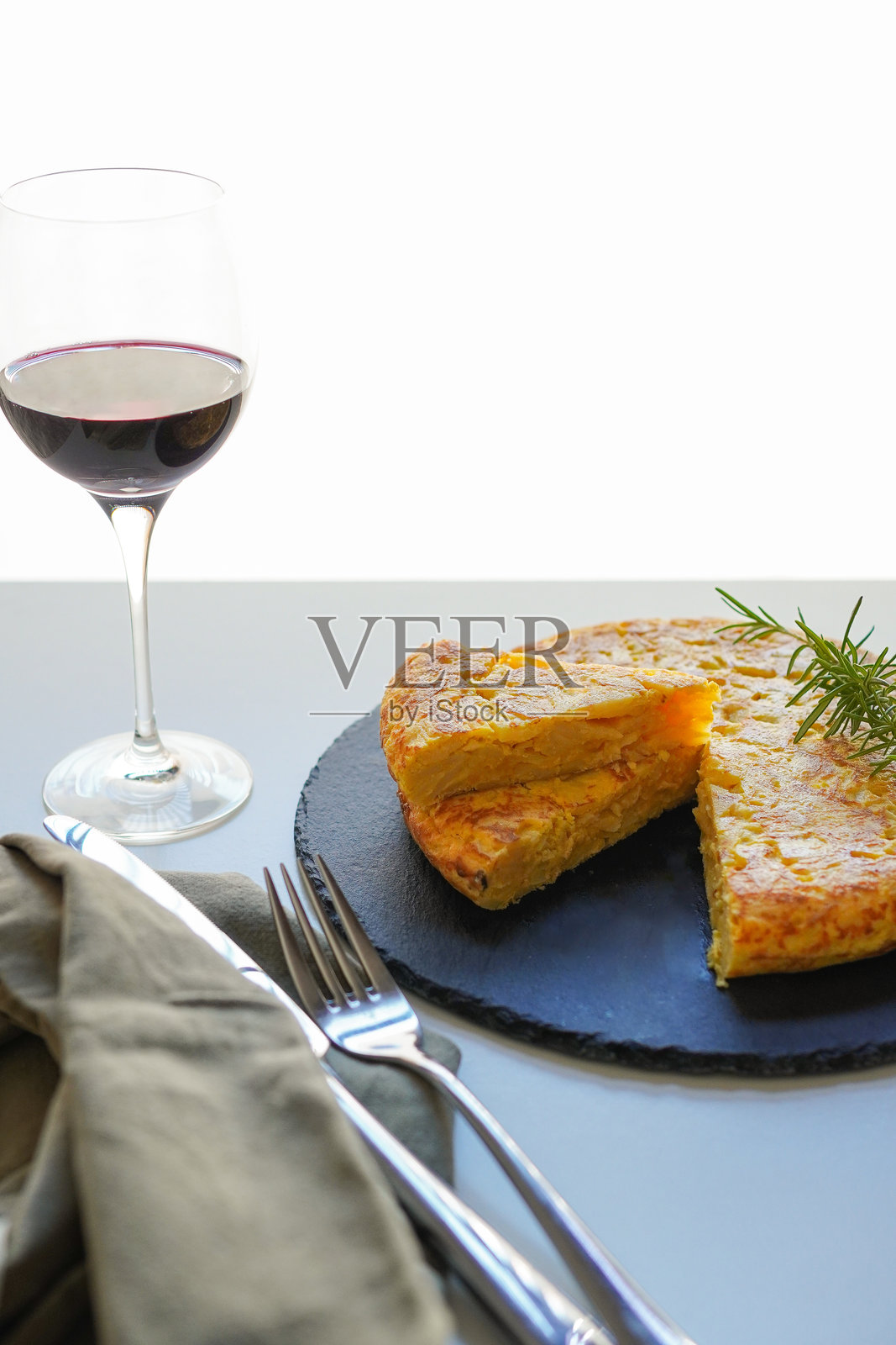 一个切好的自制西班牙土豆煎蛋卷（tortilla de patatas）放在黑色盘子上，旁边还有一杯红酒照片摄影图片