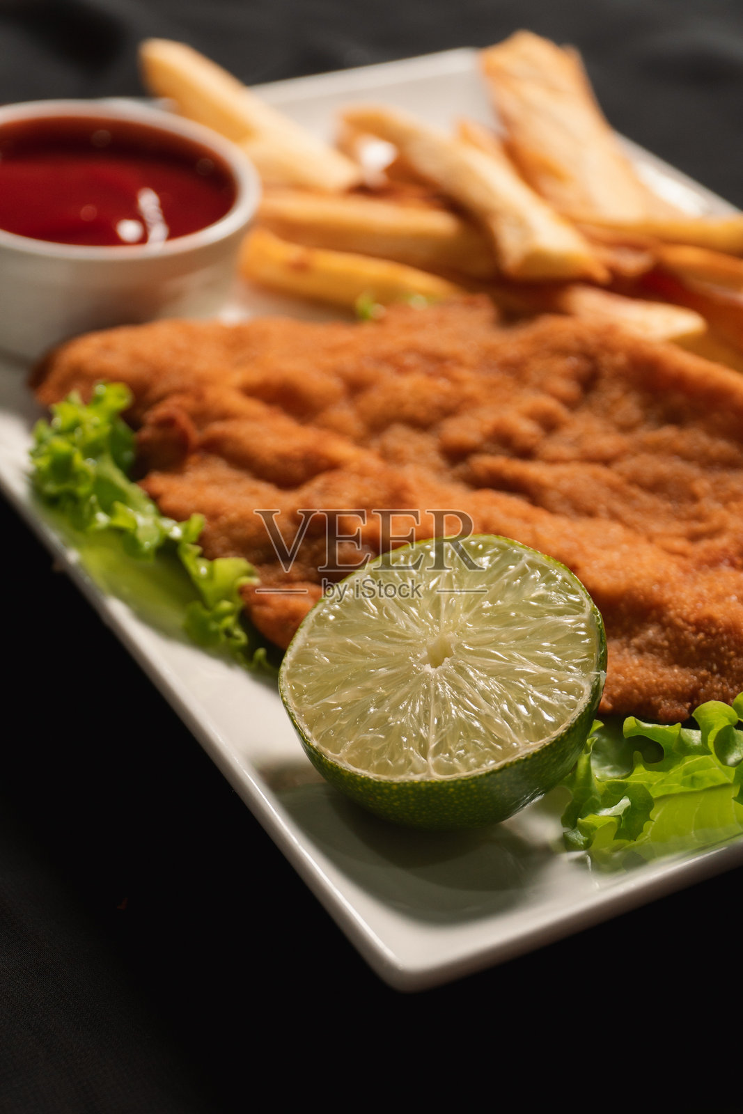 半个柠檬，背景是炸肉排和炸薯条。照片摄影图片