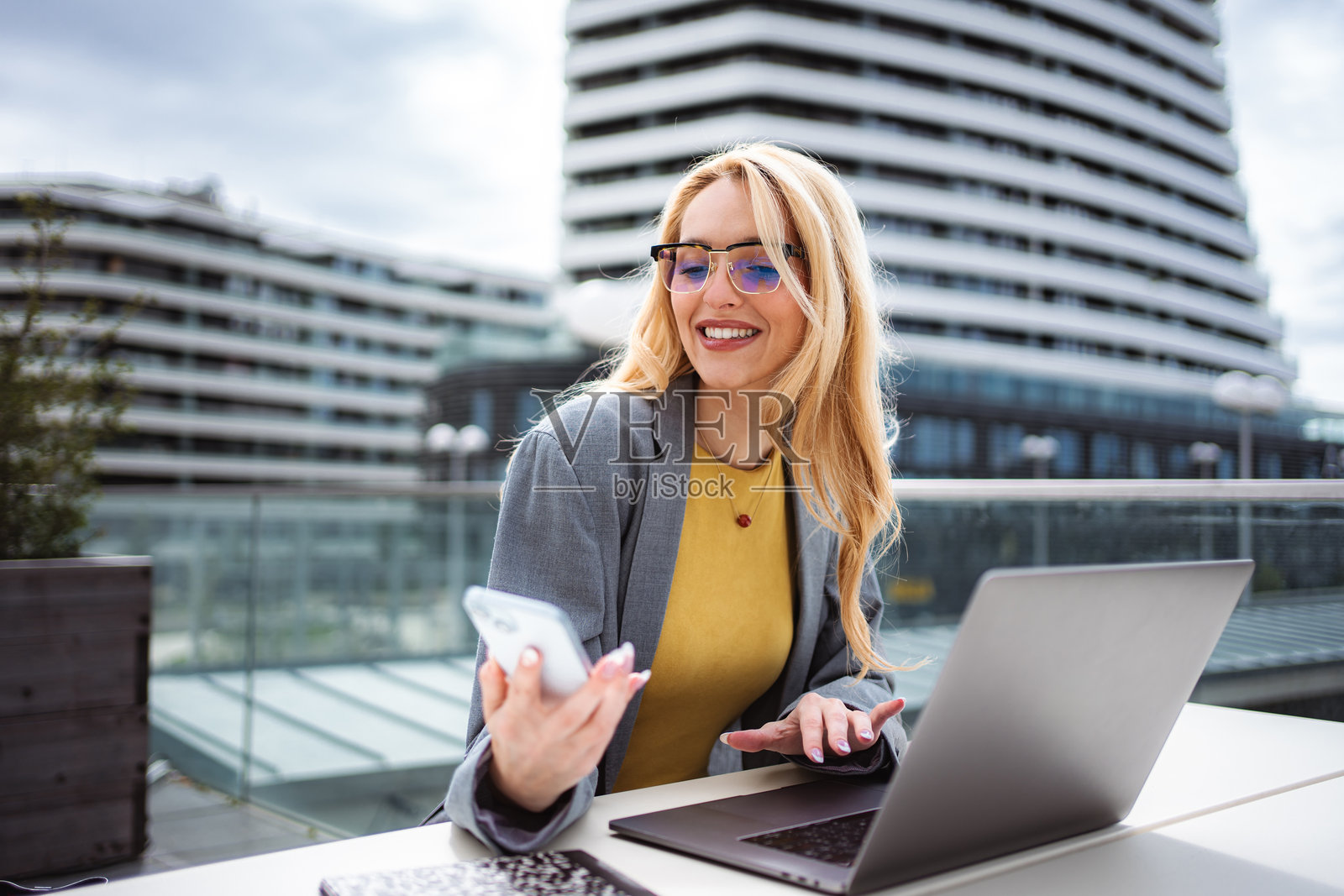 一位女士在城市的露台上边使用手机和笔记本电脑边微笑着照片摄影图片