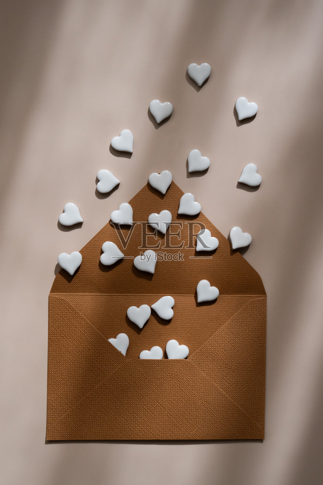棕色信封上放着白色陶瓷心形，背景为米色，极简浪漫的平面布置，带有柔和的阴影。情人节构图照片摄影图片