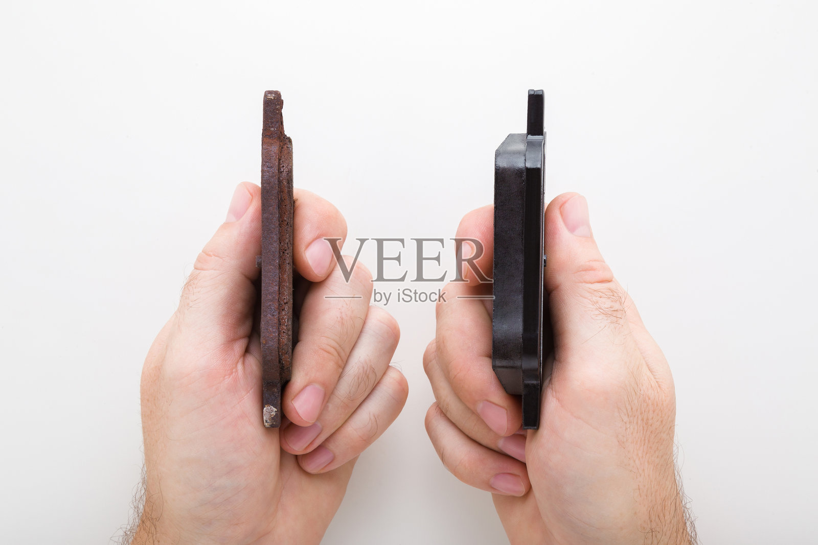 年轻男子手持全新和旧的生锈刹车片，放在浅灰色桌子背景上。展示厚薄细节。对比两个物体。汽车零配件。特写。主观视角拍摄。俯视角度。照片摄影图片