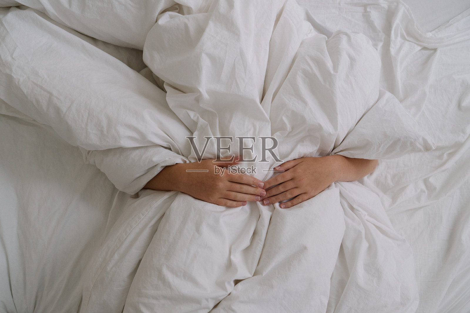 双手的舒适景象，手搭在柔软的白色床单下。极简美学象征着舒适、放松、休息和宁静的睡眠。照片摄影图片