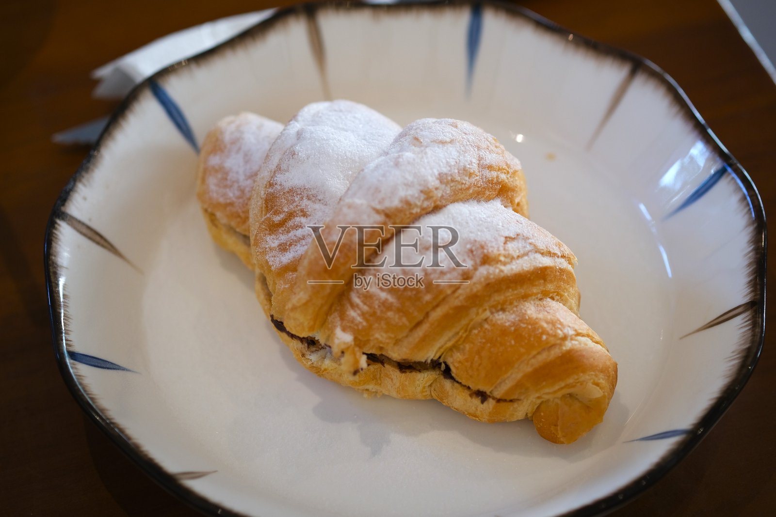 撒了糖粉的酥皮可颂，内含巧克力，盛放在一家舒适咖啡馆的陶瓷盘中。照片摄影图片