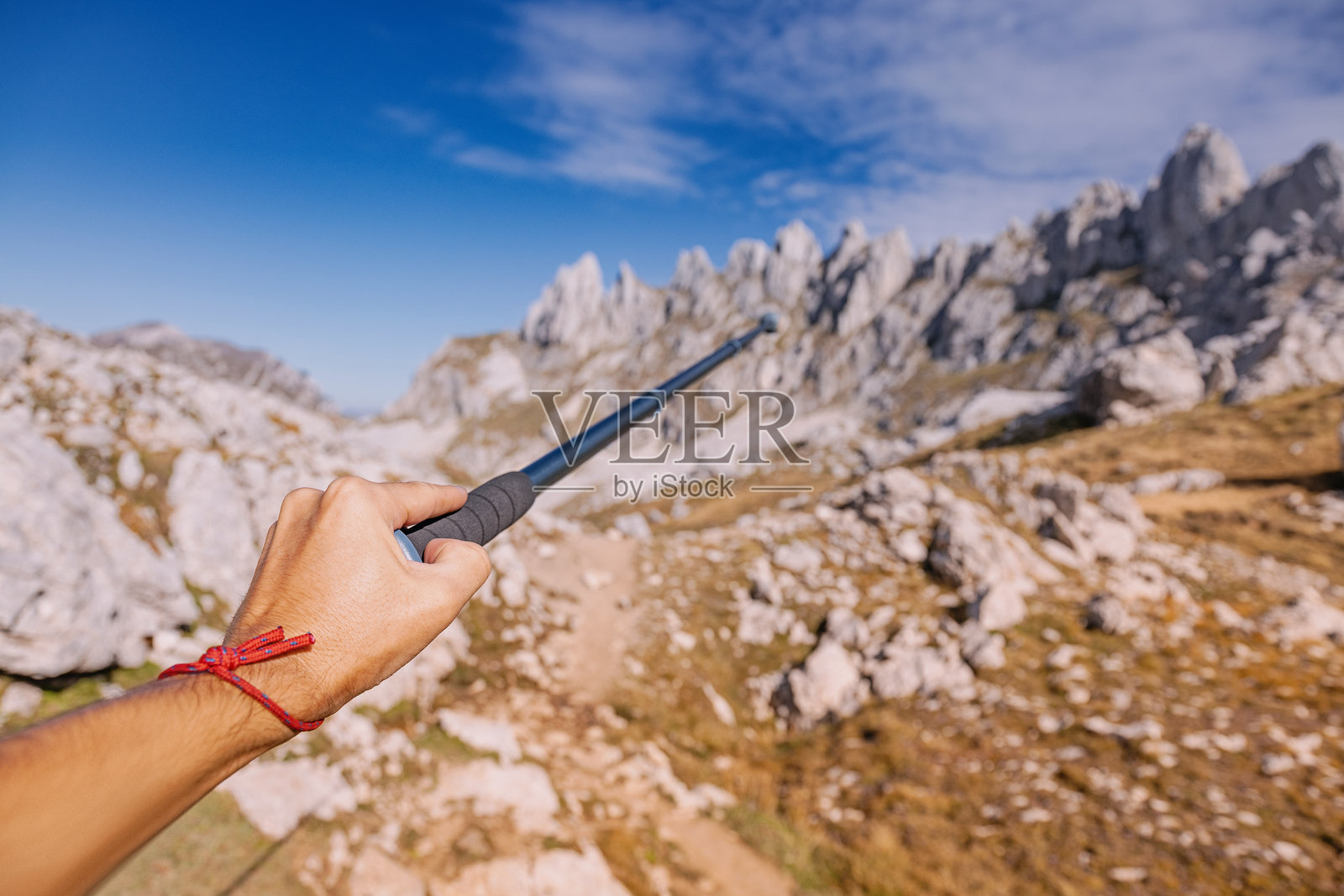 一只手拿着登山杖指向国家公园的山峰，徒步装备概念照片摄影图片