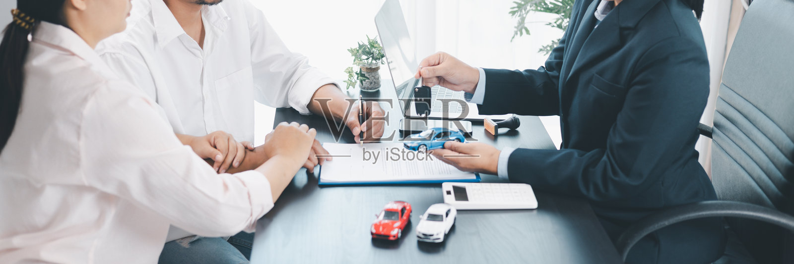 汽车经销商在签署合同期间将钥匙和车型模型交给客户的全景视图，代表着汽车贷款、金融、租赁、保险、购买协议和商业成功的概念。汽车贷款。照片摄影图片