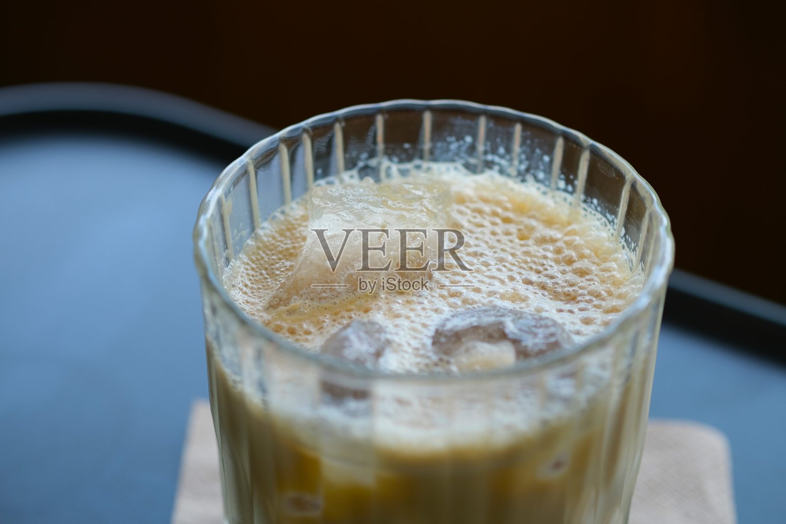 一款清爽的冰咖啡，加入牛奶，盛放在有纹理的玻璃杯中，放在棕色餐巾上，置于深色桌面。照片摄影图片