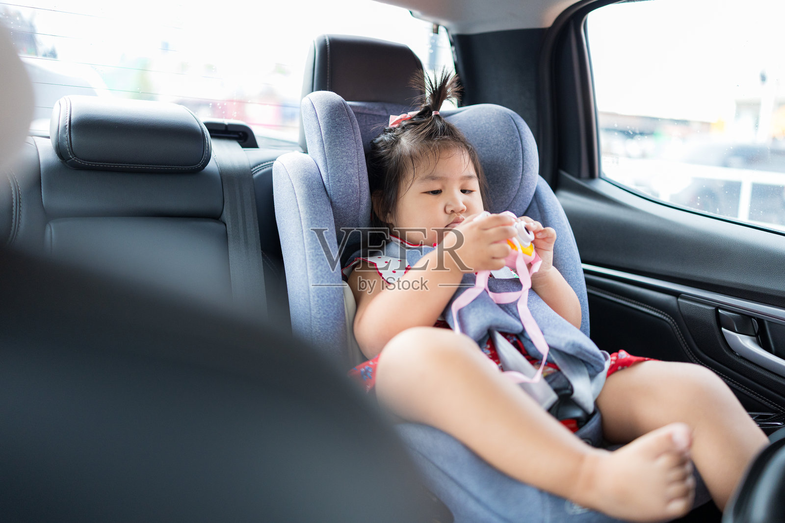 一个可爱的亚洲小女孩在旅行途中，坐在汽车后座玩着玩具相机。照片摄影图片