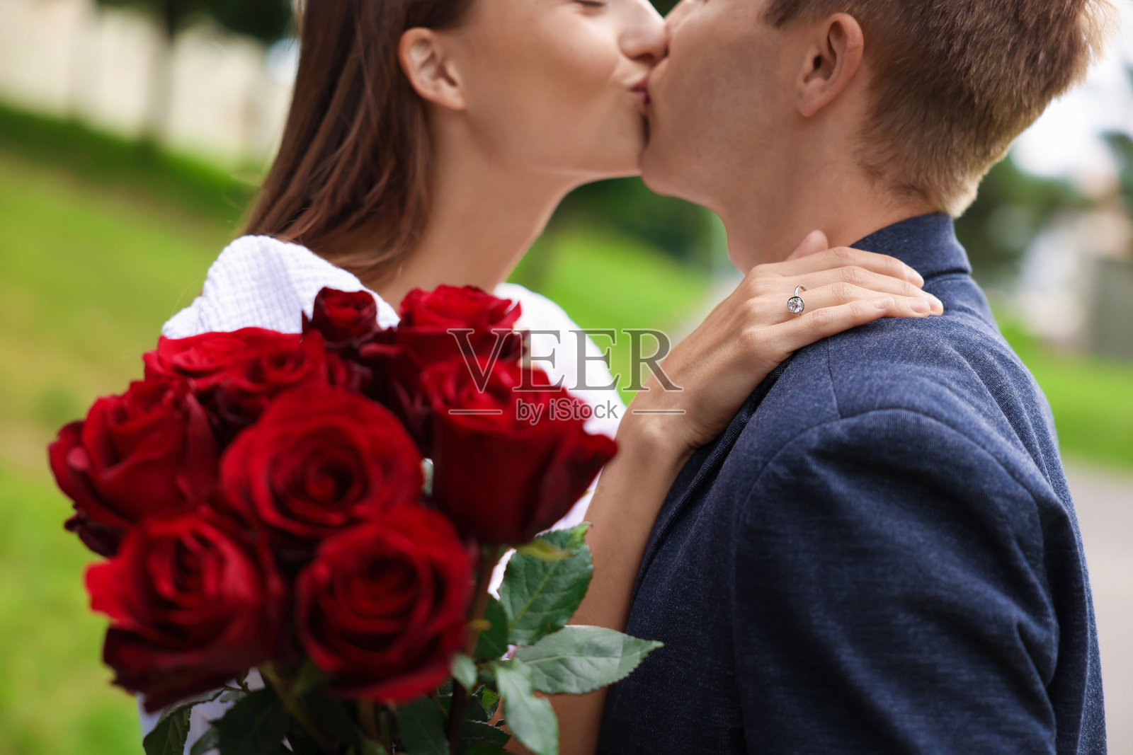求婚。男子在户外深情亲吻爱人，展示订婚戒指和玫瑰花束，特写镜头照片摄影图片