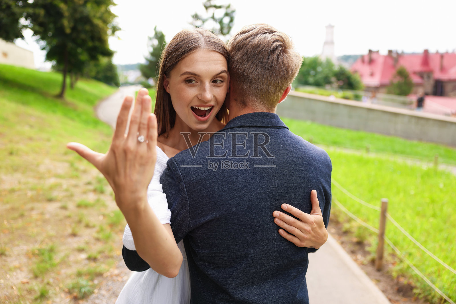 求婚。激动万分的女子抱着订婚戒指拥抱她的未婚夫，背景在户外照片摄影图片