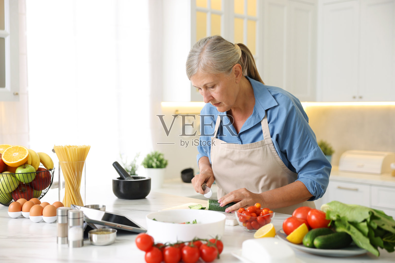 一位年长的女性在厨房的白色大理石桌上烹饪照片摄影图片