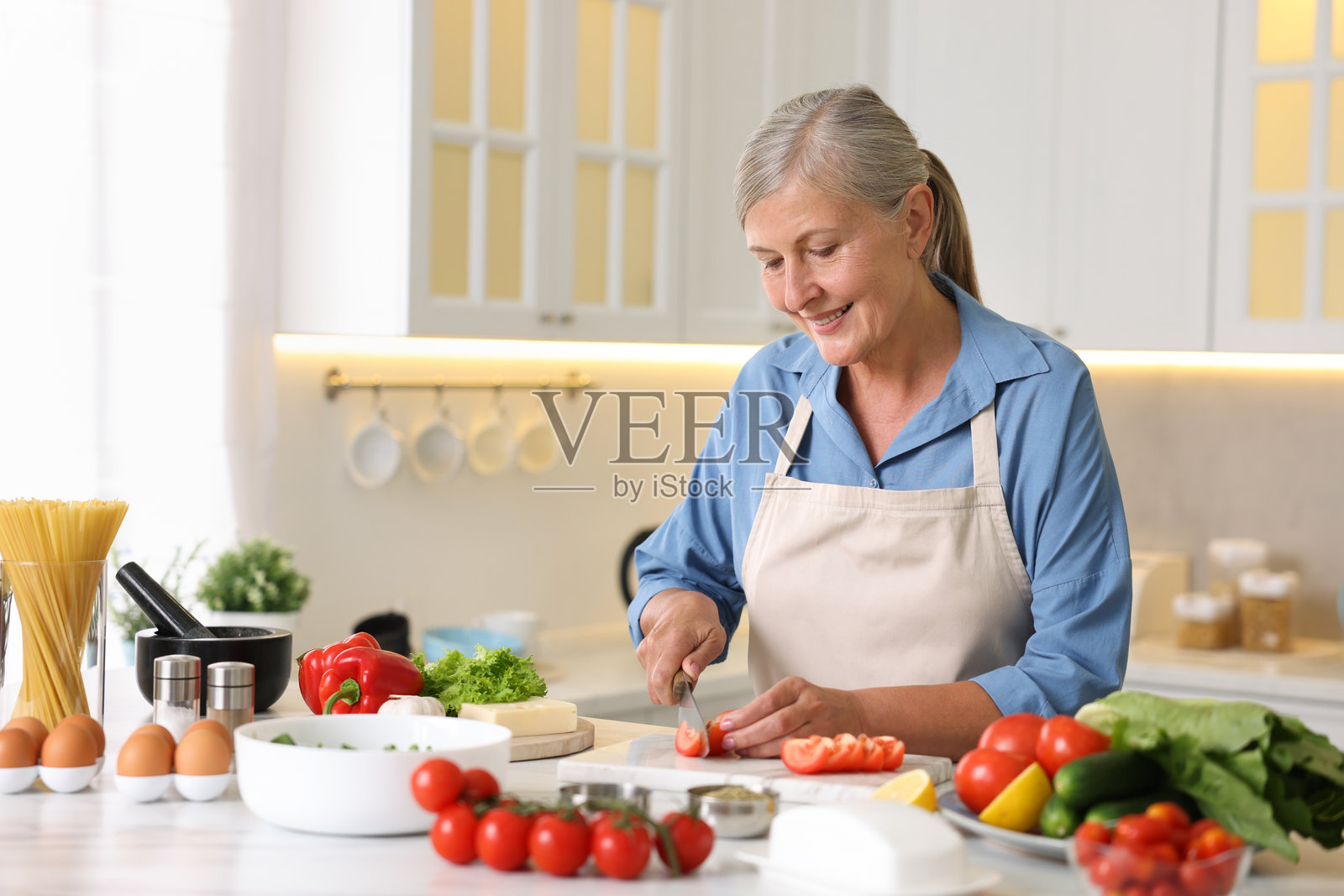 一位年长的女性在厨房的白色大理石桌上烹饪照片摄影图片