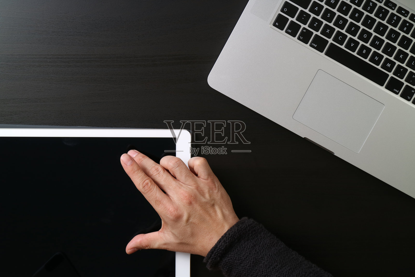 黑暗的书桌上，一只手正在使用平板电脑，旁边是笔记本电脑照片摄影图片