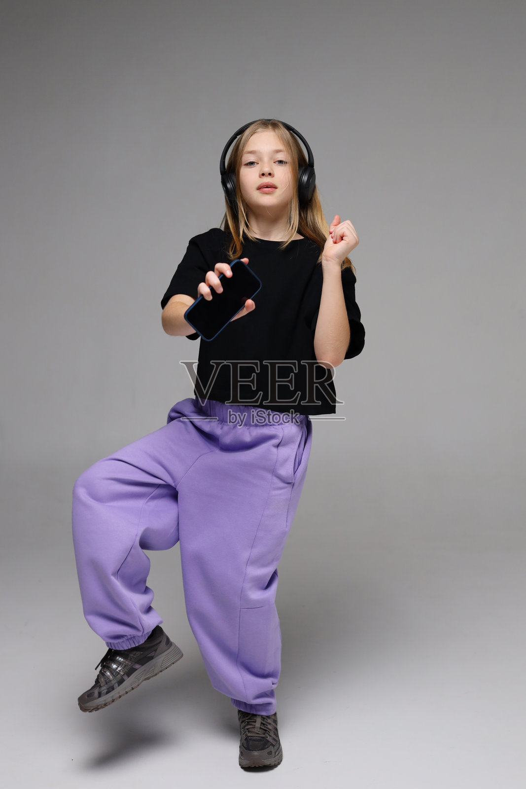 年轻的高加索女孩在录音室里戴着耳机，拿着智能手机跳舞照片摄影图片