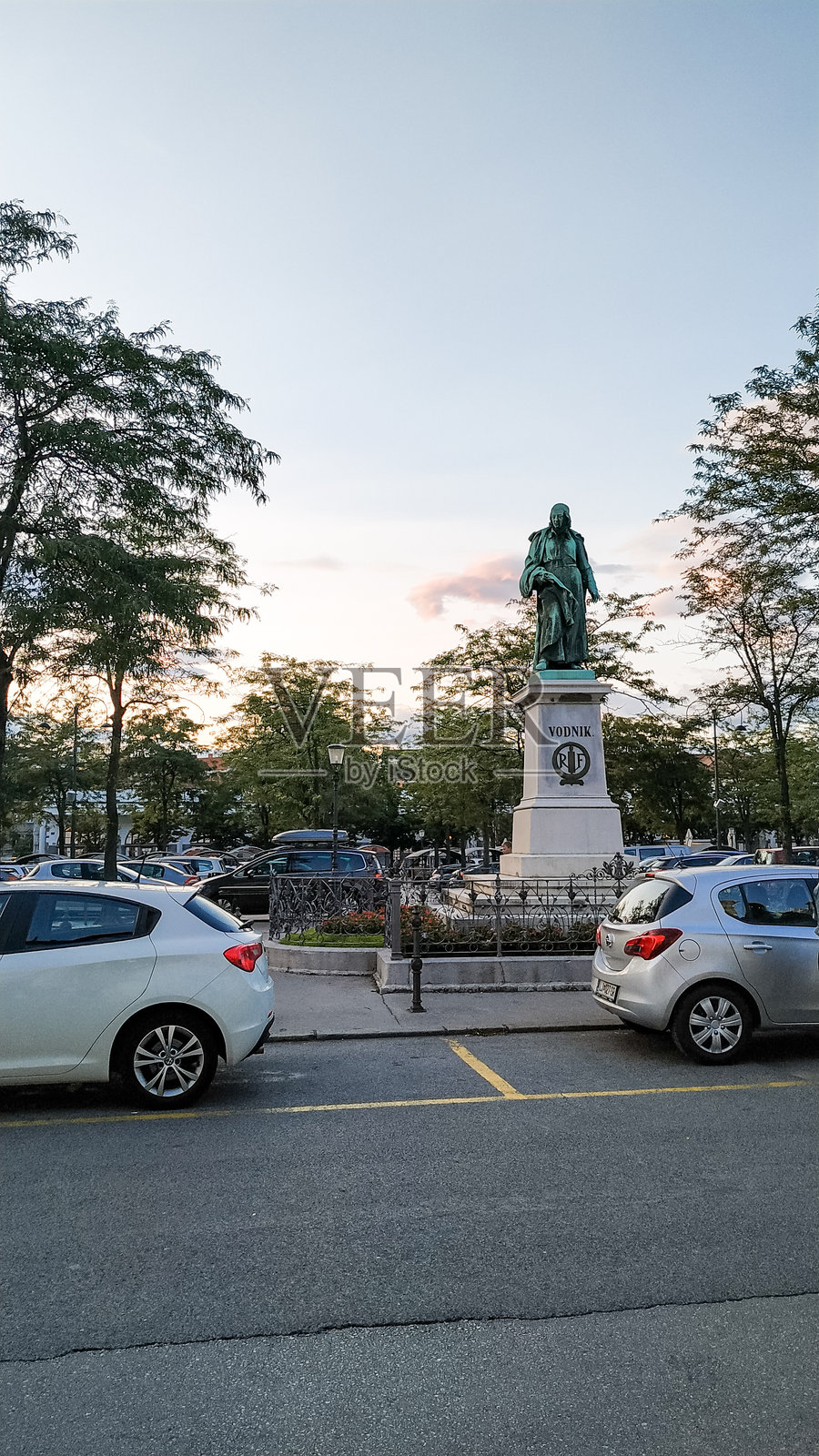 城市公园里的历史人物雕像，有车辆和树木。照片摄影图片