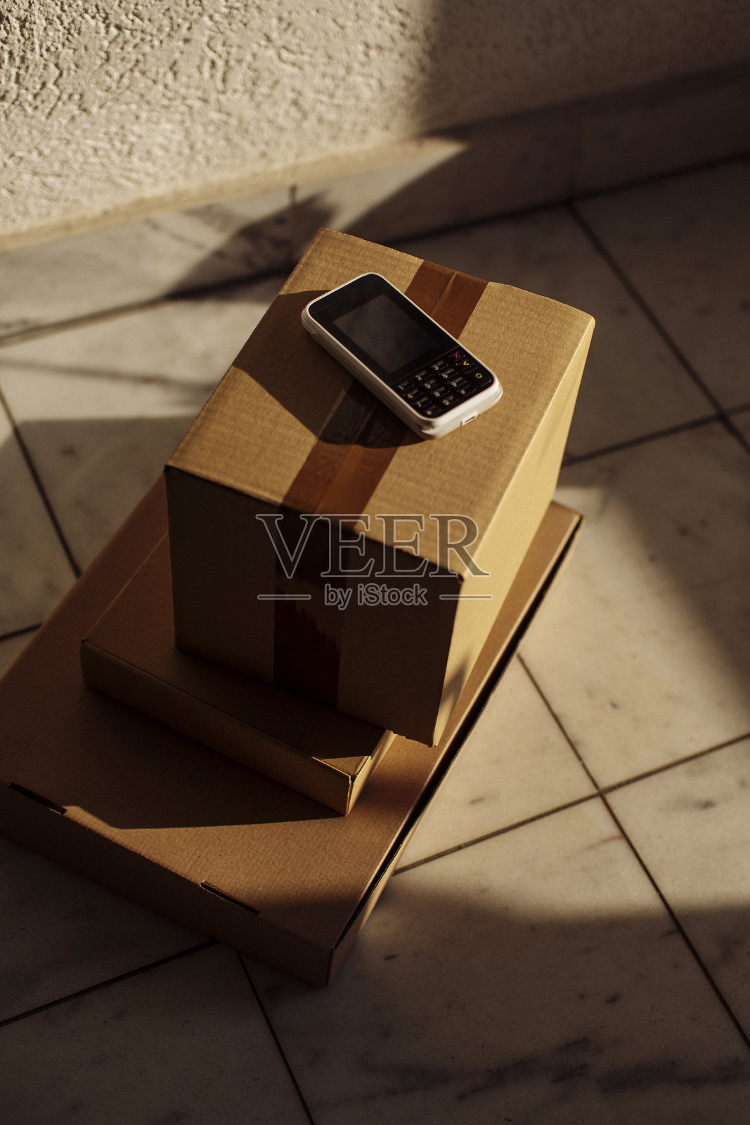在瓷砖地板上，一部手机放在纸板箱上，沐浴在温暖的阳光下照片摄影图片
