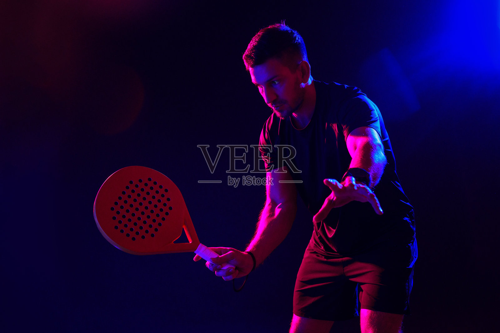 在室内球场，男人在彩色灯光下打板式网球照片摄影图片