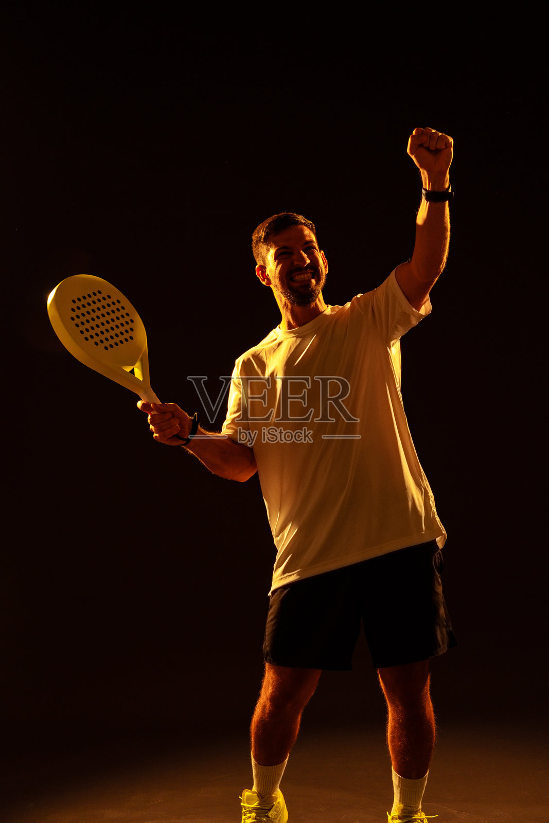 一名男子在戏剧性的灯光下挥舞着球拍庆祝胜利照片摄影图片
