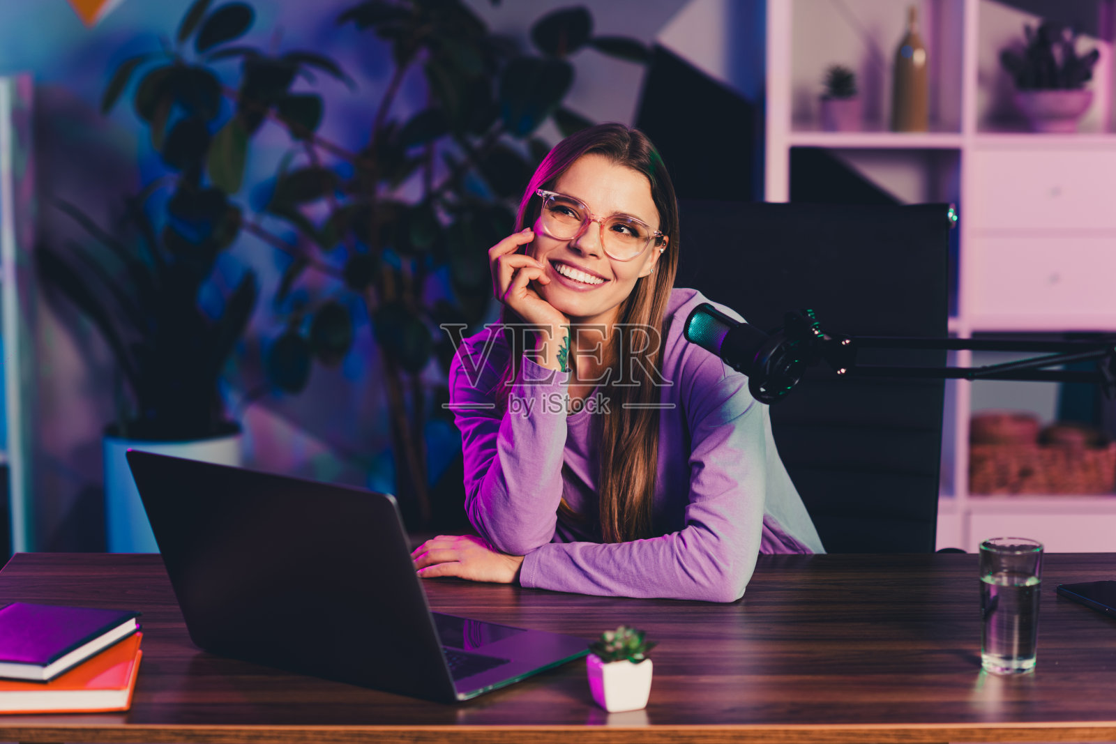 身着休闲装的内容创作者坐在书桌前，配备麦克风和笔记本电脑，在一个充满活力的家庭办公室环境中进行交谈照片摄影图片
