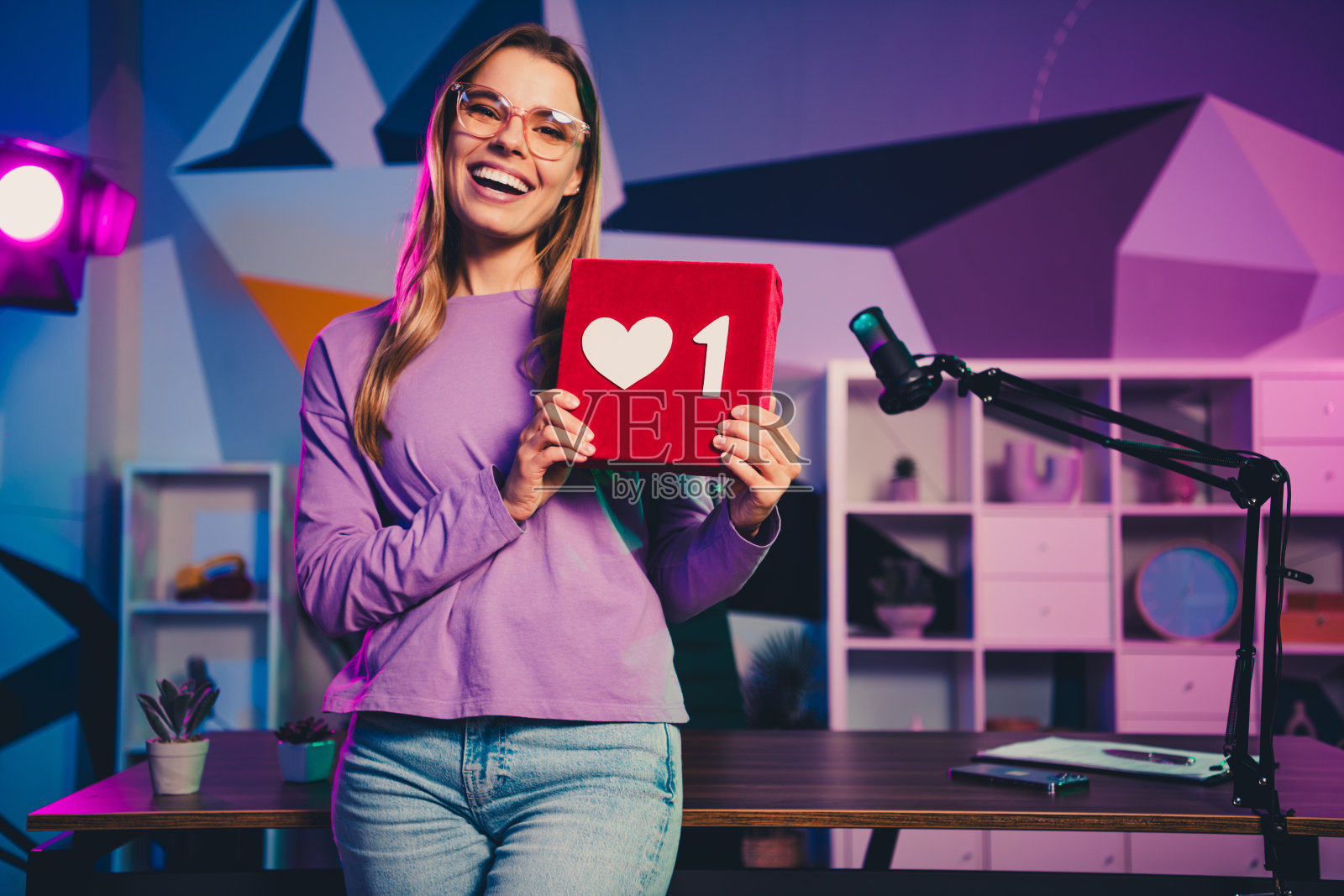 微笑的女性在色彩缤纷的影棚中手持爱心手势，象征社交媒体互动或内容创作照片摄影图片
