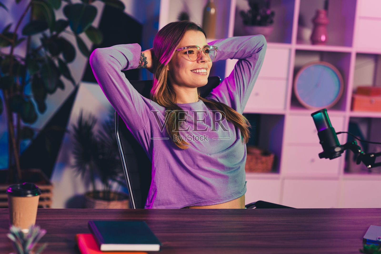 迷人的女性在发光的霓虹灯下享受她的创意工作空间，配有麦克风，用于直播和播客录制。照片摄影图片