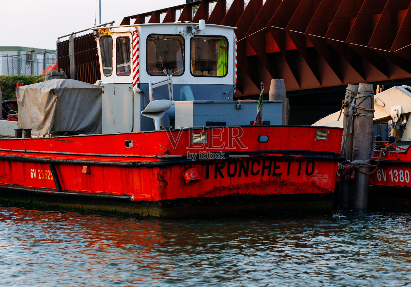 红色的“Tronchetto”号拖船停靠在码头，展示着鲜艳的色彩和水中的倒影，代表着海运和工业。照片摄影图片