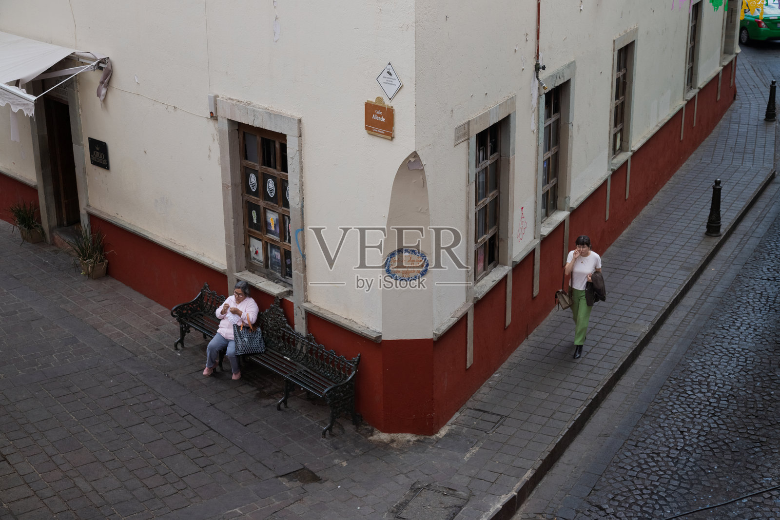 一位年迈的女士独自坐在亚连德街的长椅上，另一位女士走过历史中心照片摄影图片