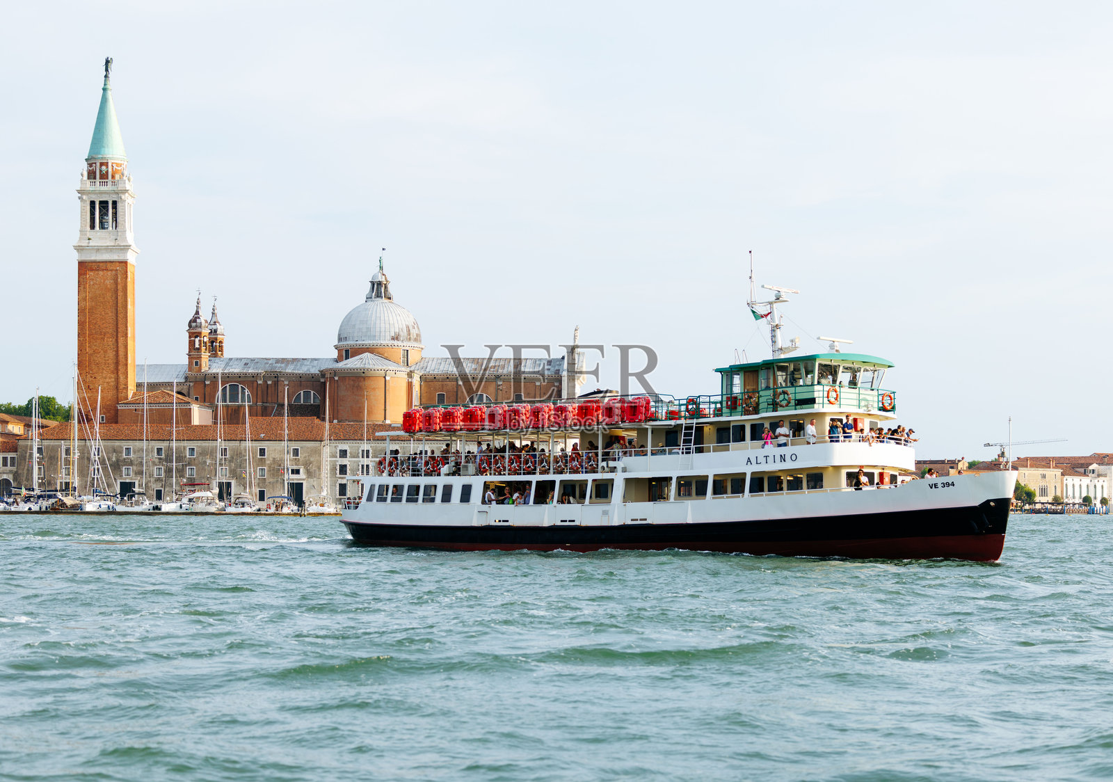 名为“亚历西奥”的渡轮载着游客穿越大运河，背景是威尼斯历史建筑和钟楼，展现了这座城市的魅力照片摄影图片