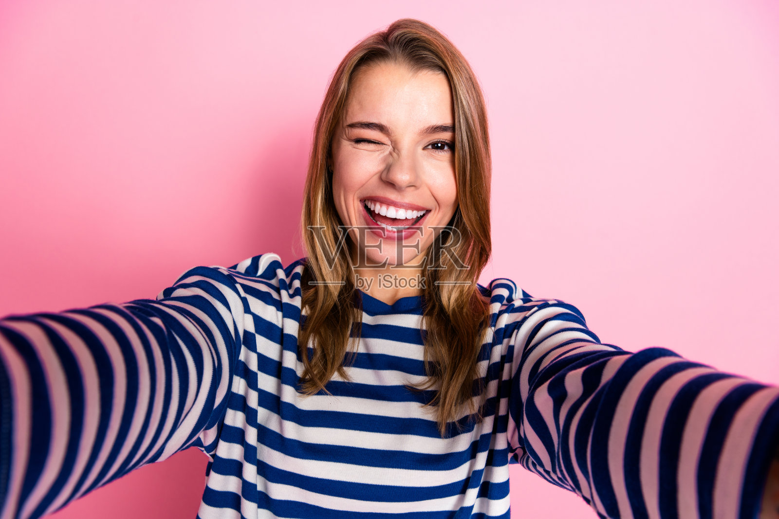 一位身穿休闲条纹毛衣的年轻女子，面带笑容，在纯粉色背景前愉快地摆姿势，适合休闲或生活方式类图片照片摄影图片