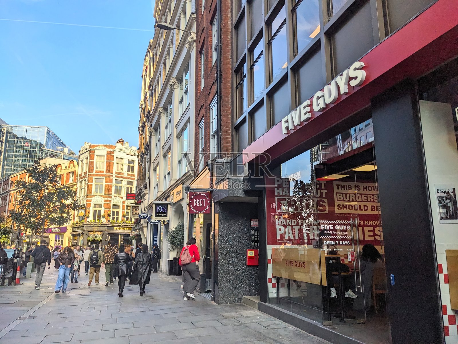 行人走过伦敦市中心阳光明媚的毕晓普斯盖特街上的一家Five Guys餐厅照片摄影图片