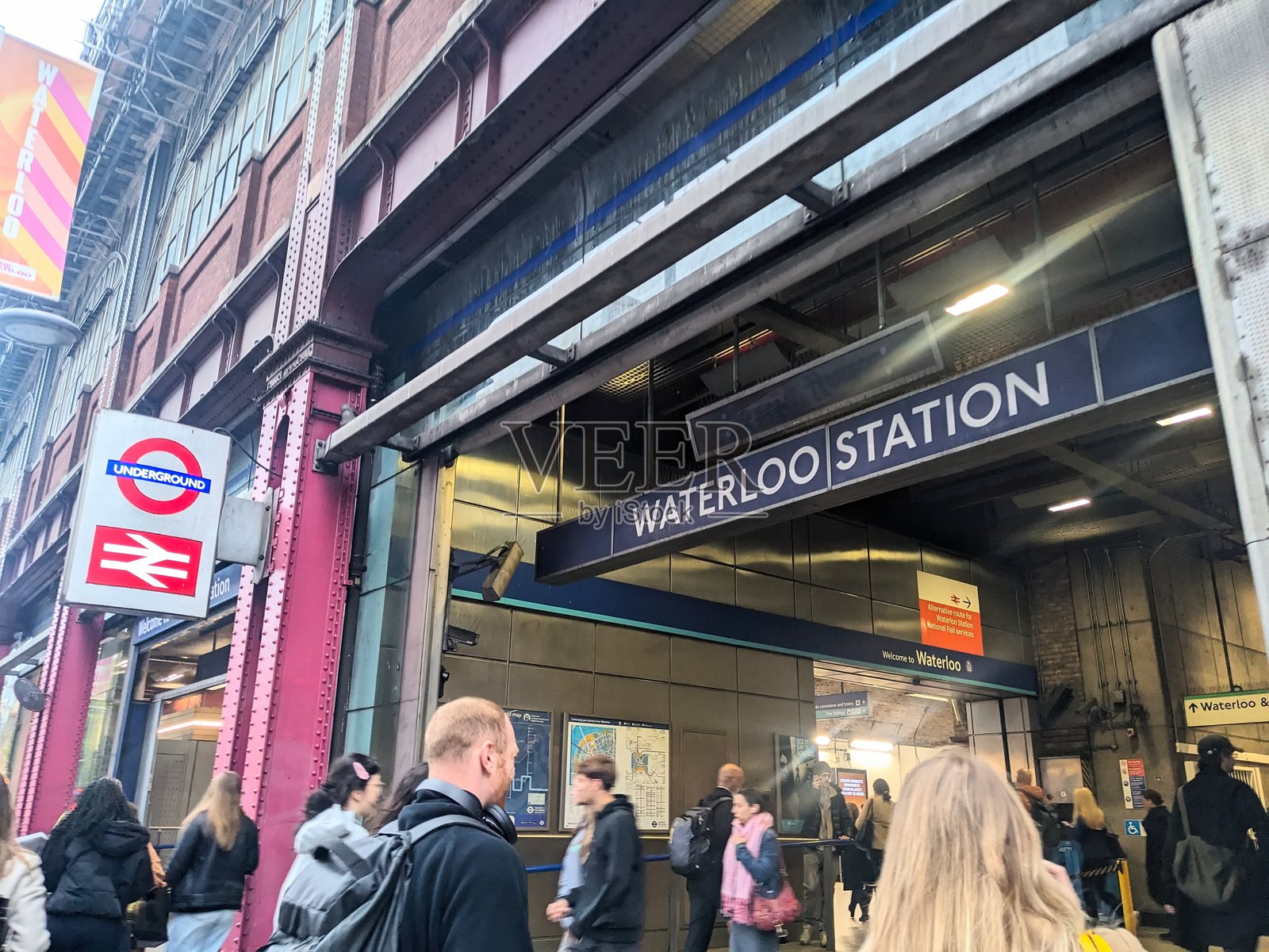 通勤者进入繁忙的滑铁卢火车站入口,入口处有标志性的伦敦地铁圆形标志照片摄影图片