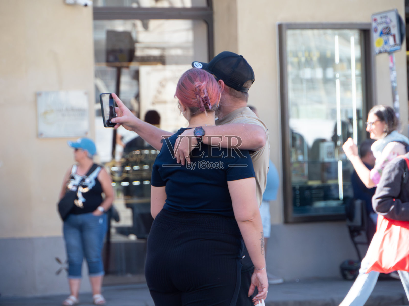 一对情侣在意大利比萨奇迹广场游览时,拥抱并用智能手机自拍照片摄影图片