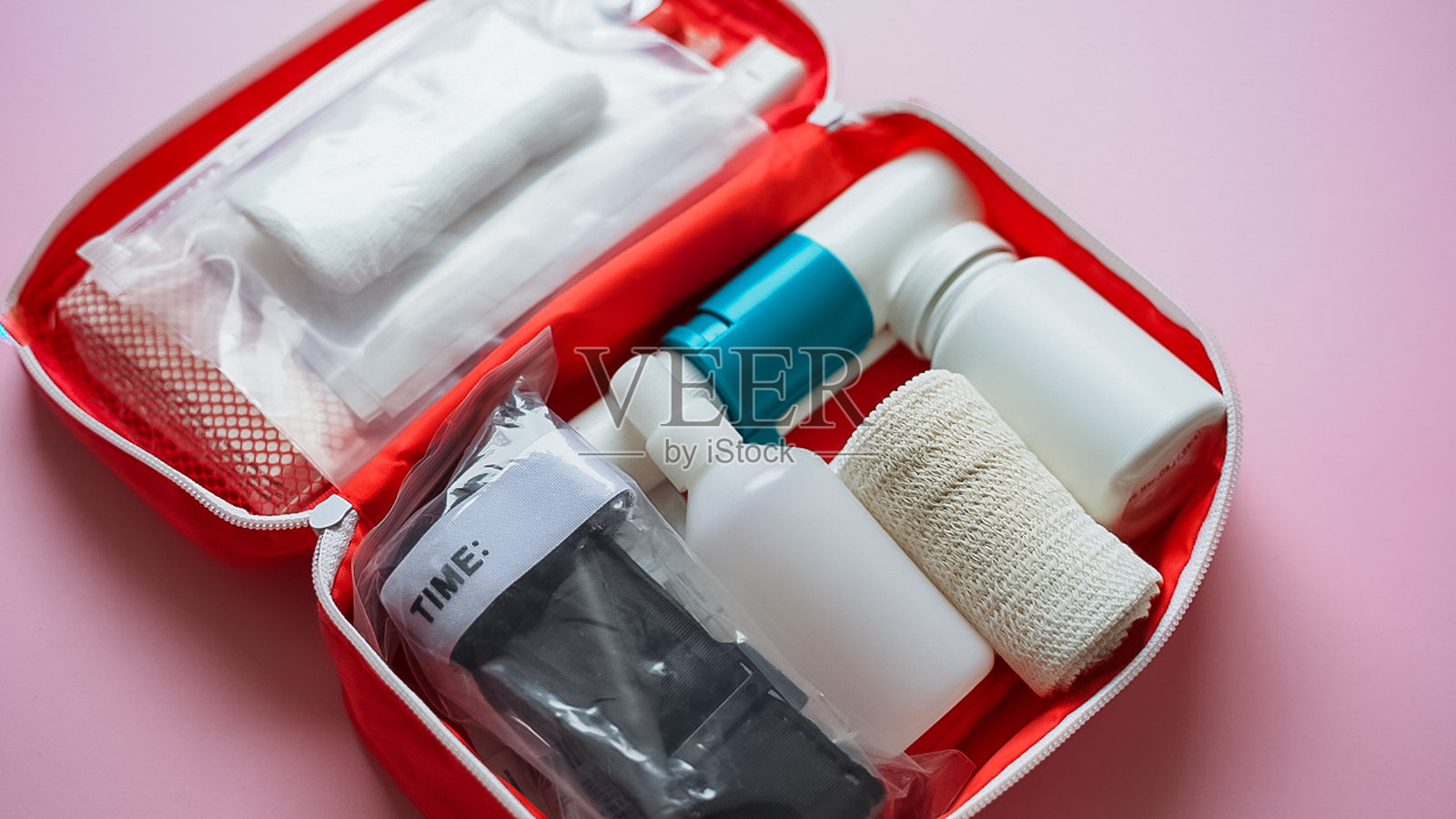 一个装满了各种瓶子和绷带的鲜红色急救箱，背景是充满活力的粉红色，增添了愉悦感照片摄影图片