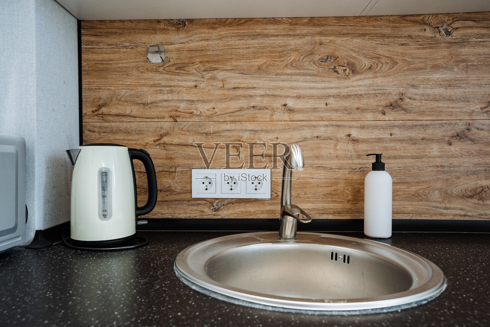 在一个温馨舒适的厨房里，一个设计精美的洗碗池旁放着一个迷人的烧水壶，实用的皂液器则优雅地摆放在台面上，方便取用。照片摄影图片