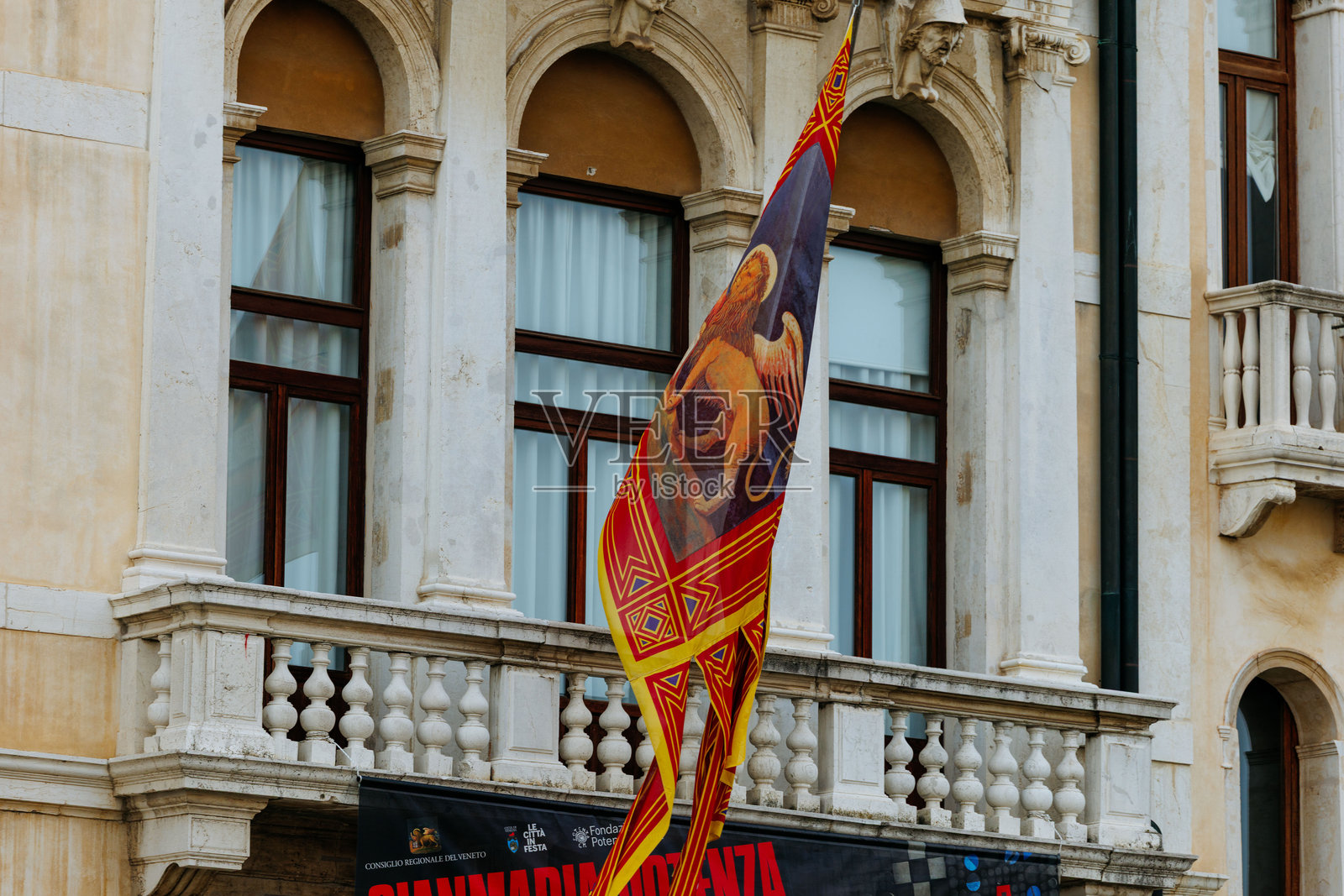 一面色彩鲜艳、设计精美的旗帜在威尼斯历史建筑前飘扬,展现了意大利威尼斯丰富的文化遗产照片摄影图片