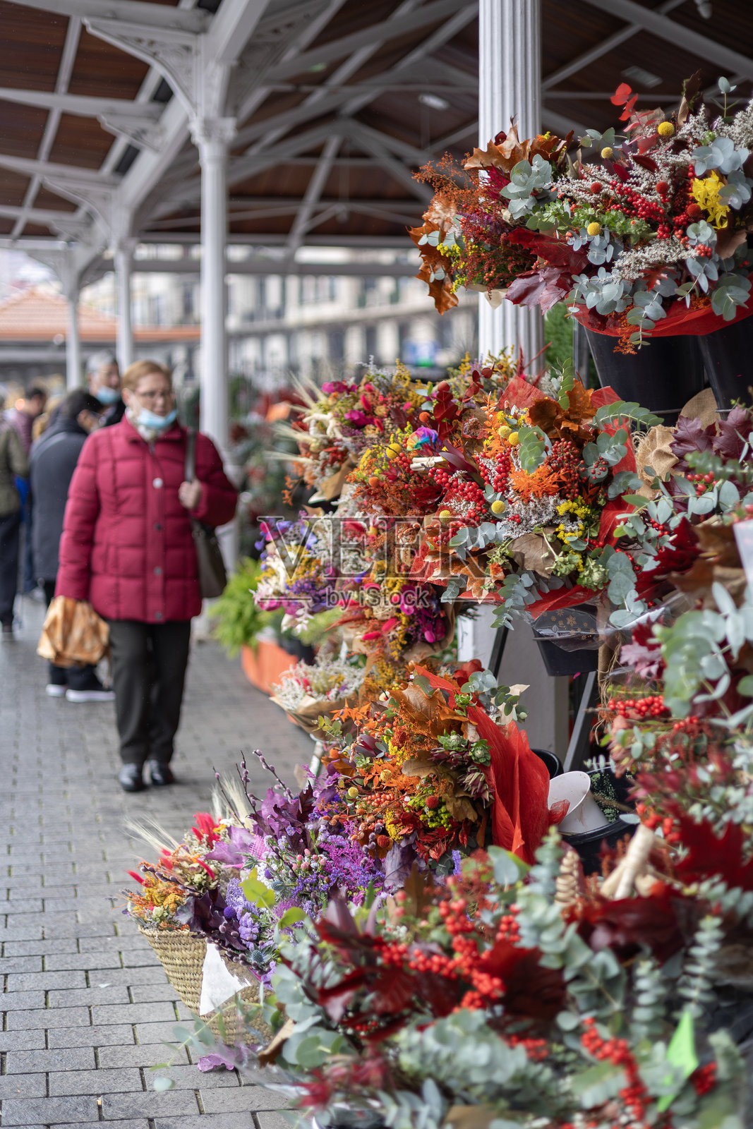 在鲜花市场出售的色彩丰富、质朴的圣诞花束（Ramos Navidenos）琳琅满目，背景中有顾客正在选购。照片摄影图片