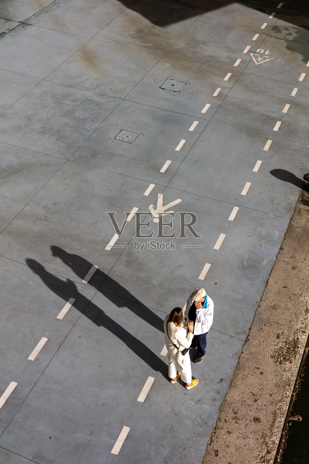 桑坦德海滨的步行和自行车道上站着两个人,在午后的阳光下投下长长的影子。照片摄影图片