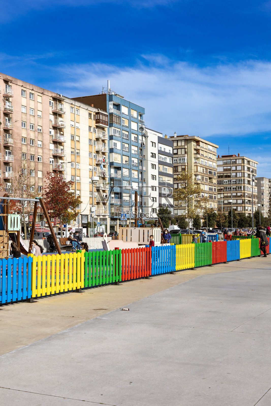 西班牙桑坦德,2021年11月19日:渔人区海滨一处儿童游乐场的彩色围栏,背景是现代化的公寓楼。照片摄影图片