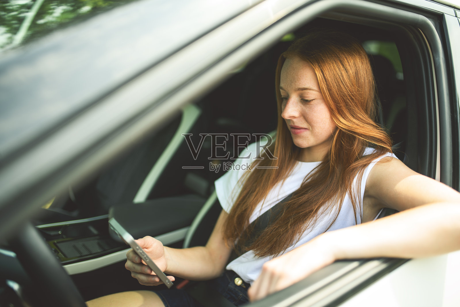 年轻漂亮的女孩司机正在用手机和她的白色汽车照片摄影图片