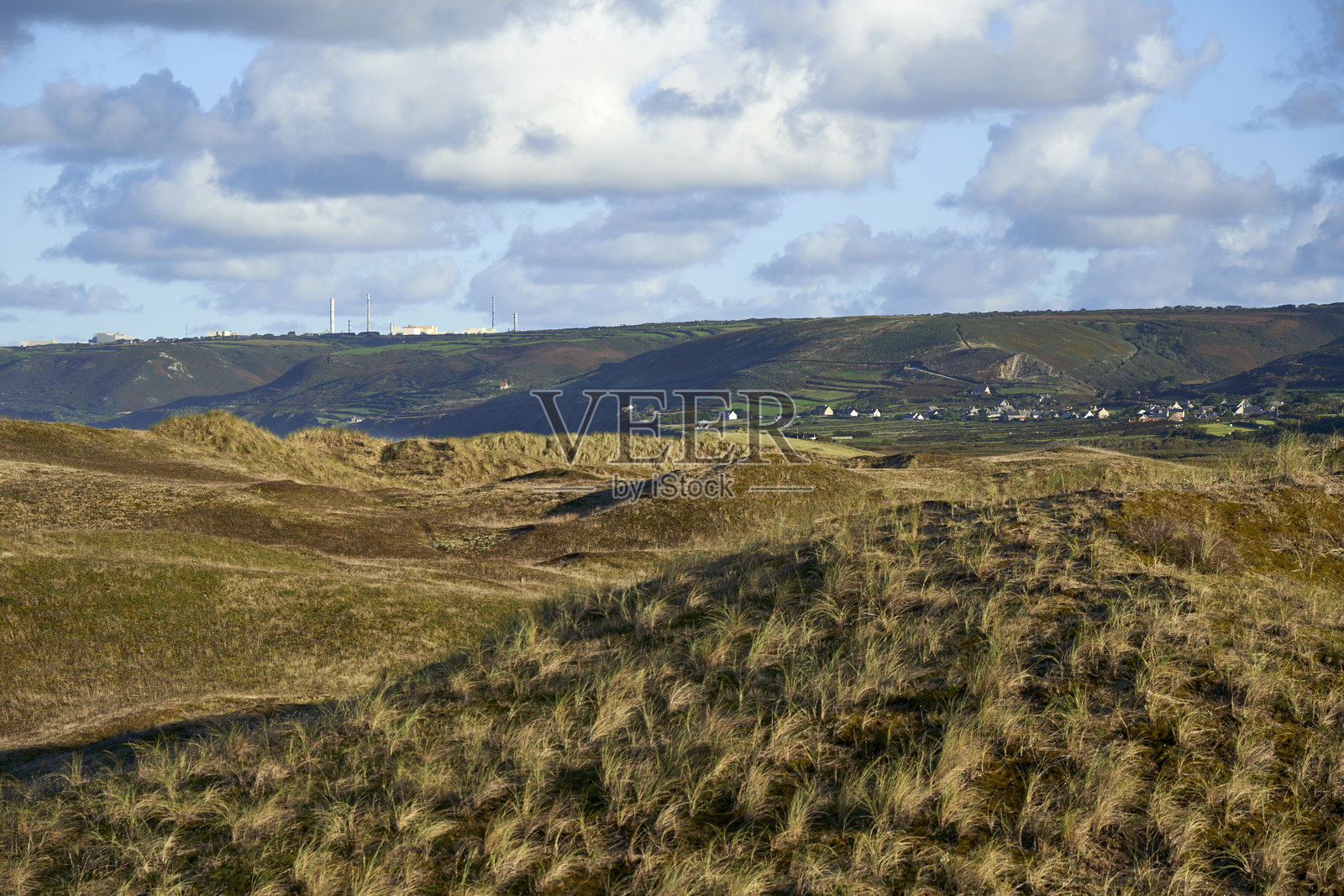 在宁静村庄附近的山区景观中，工业烟囱、再处理厂和设施坐落在绿色的田野上，天空布满云彩。法国诺曼底拉海格。照片摄影图片