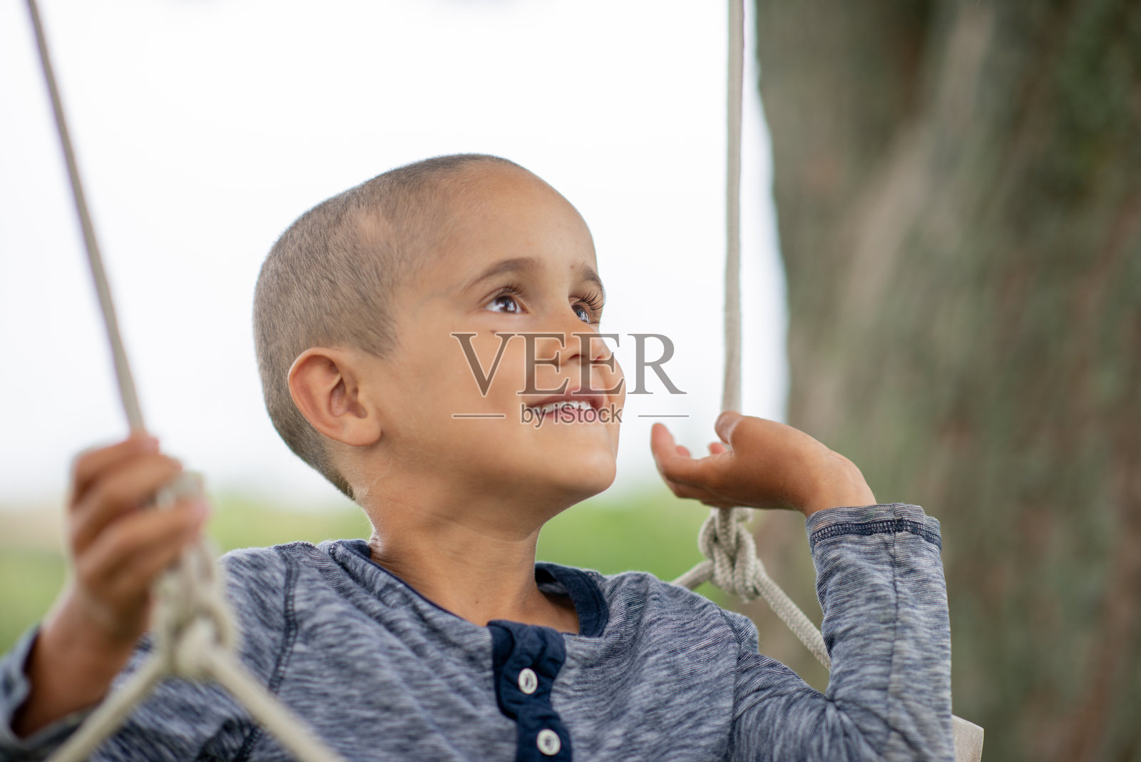 快乐的小男孩在户外荡秋千，仰头望着，脸上带着灿烂的笑容照片摄影图片