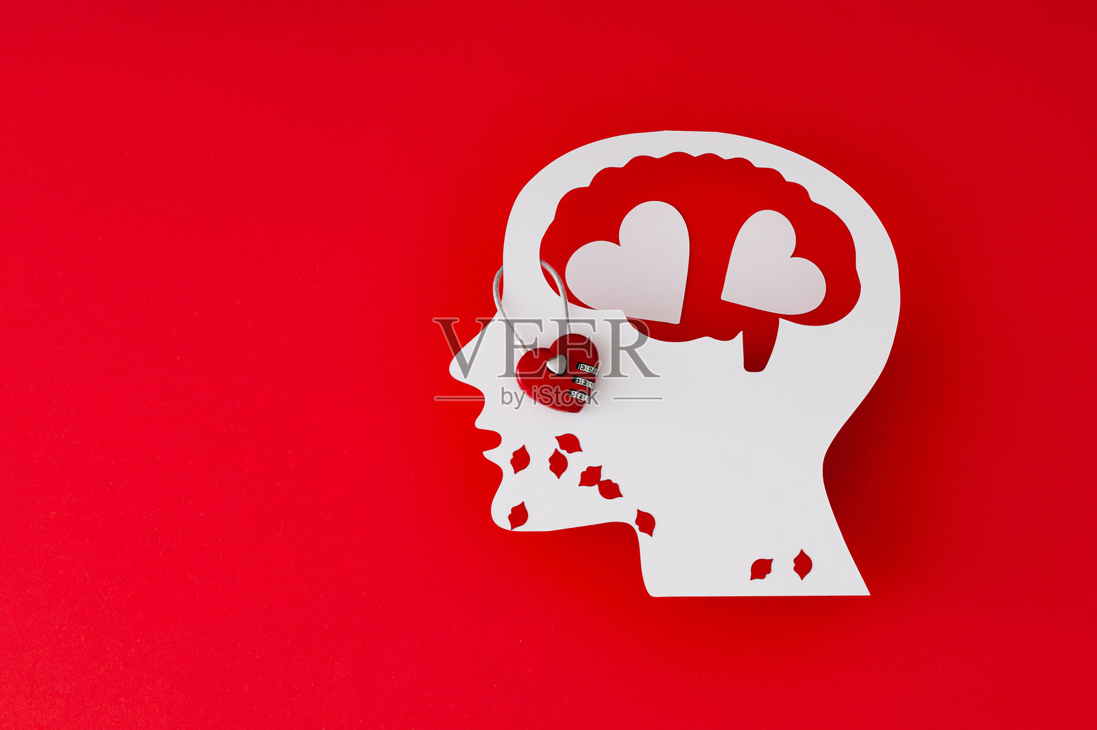 红色背景下纸质人头的侧面像，带有心形和嘴唇。头脑中的爱。浪漫情感、情商和心理健康的象征性表现。照片摄影图片