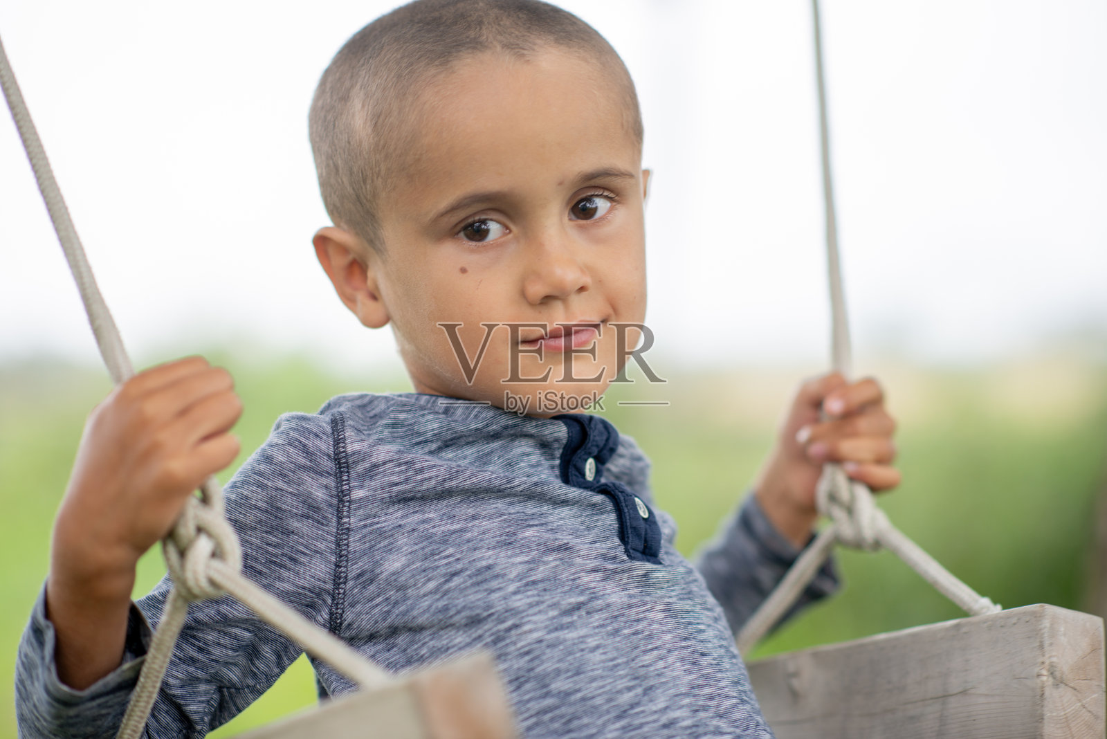 小男孩在户外公园的秋千上，表情平静，眼神专注照片摄影图片