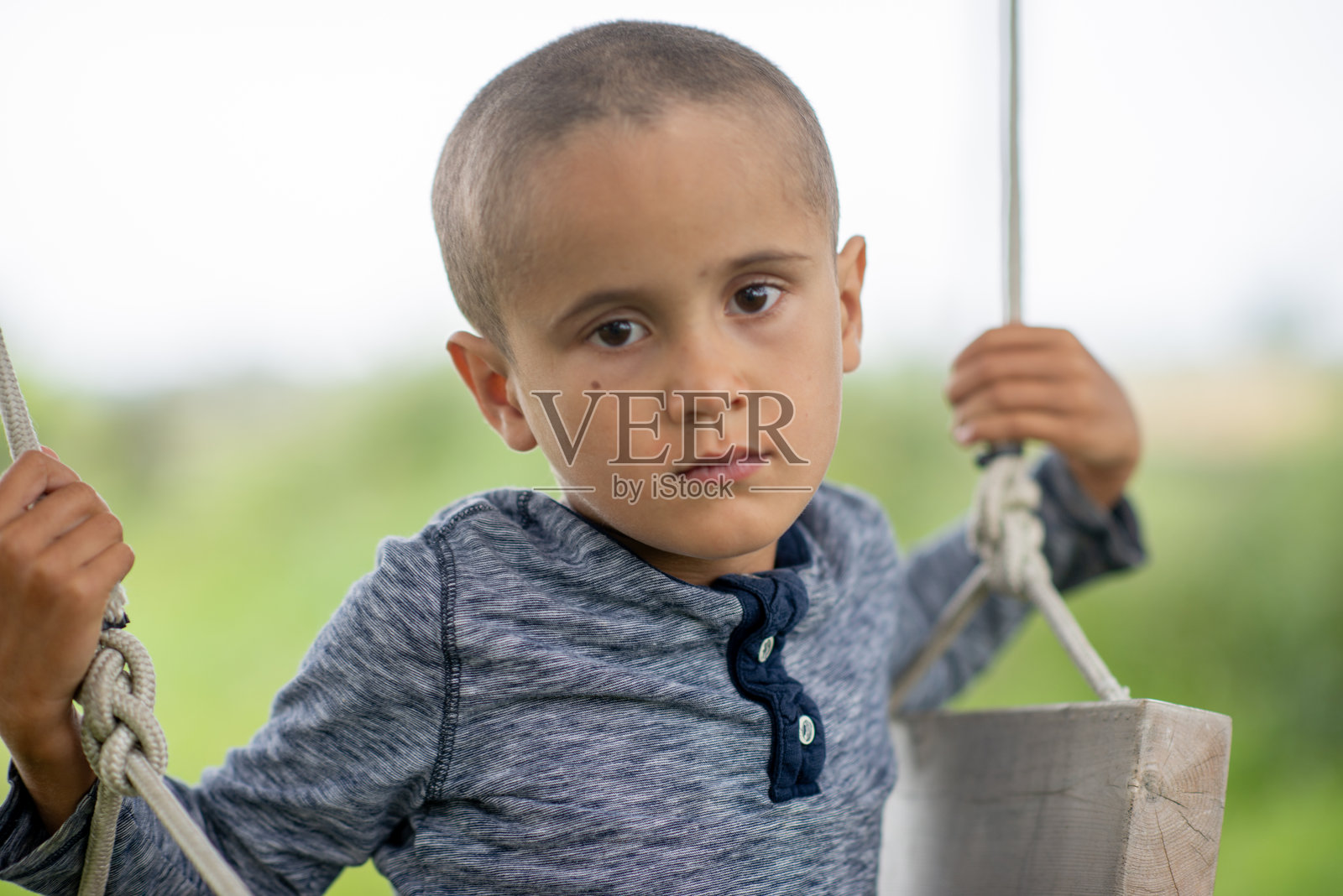 患有癌症的拉丁裔小男孩在户外荡秋千，眼神中流露出宁静的希望照片摄影图片