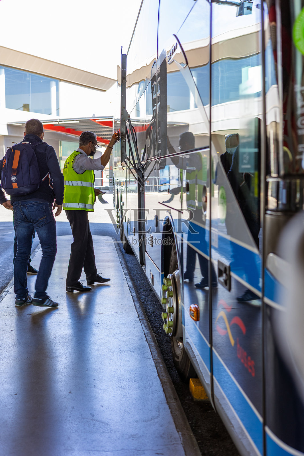 一名Alsa巴士司机在阿利坎特巴士站协助乘客搬运行李，准备前往瓦伦西亚，突显了城际交通的服务与效率。照片摄影图片