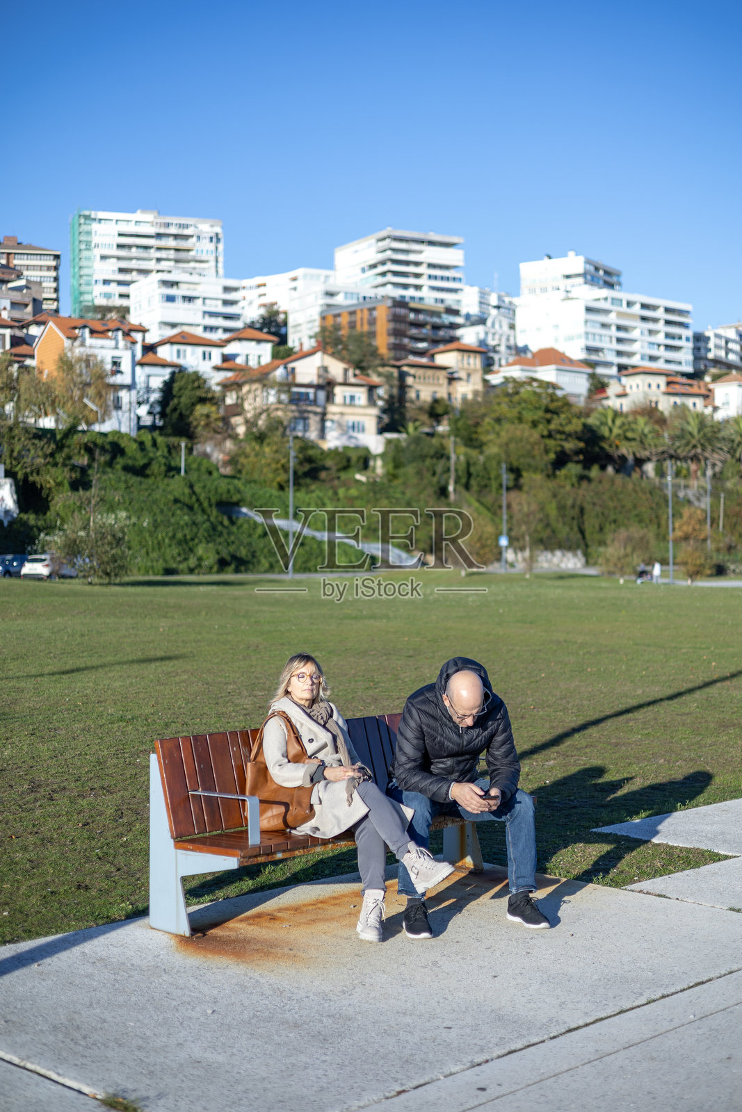 一对情侣在桑坦德的加马佐广场公园长椅上休息，背景是城市的山坡住宅区。照片摄影图片