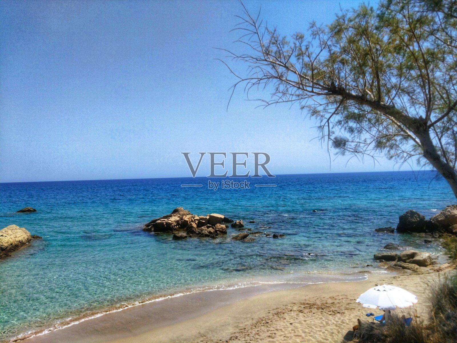 希腊克里特岛锡蒂亚附近宁静的地中海海滩，拥有绿松石色的海水和白色遮阳伞照片摄影图片