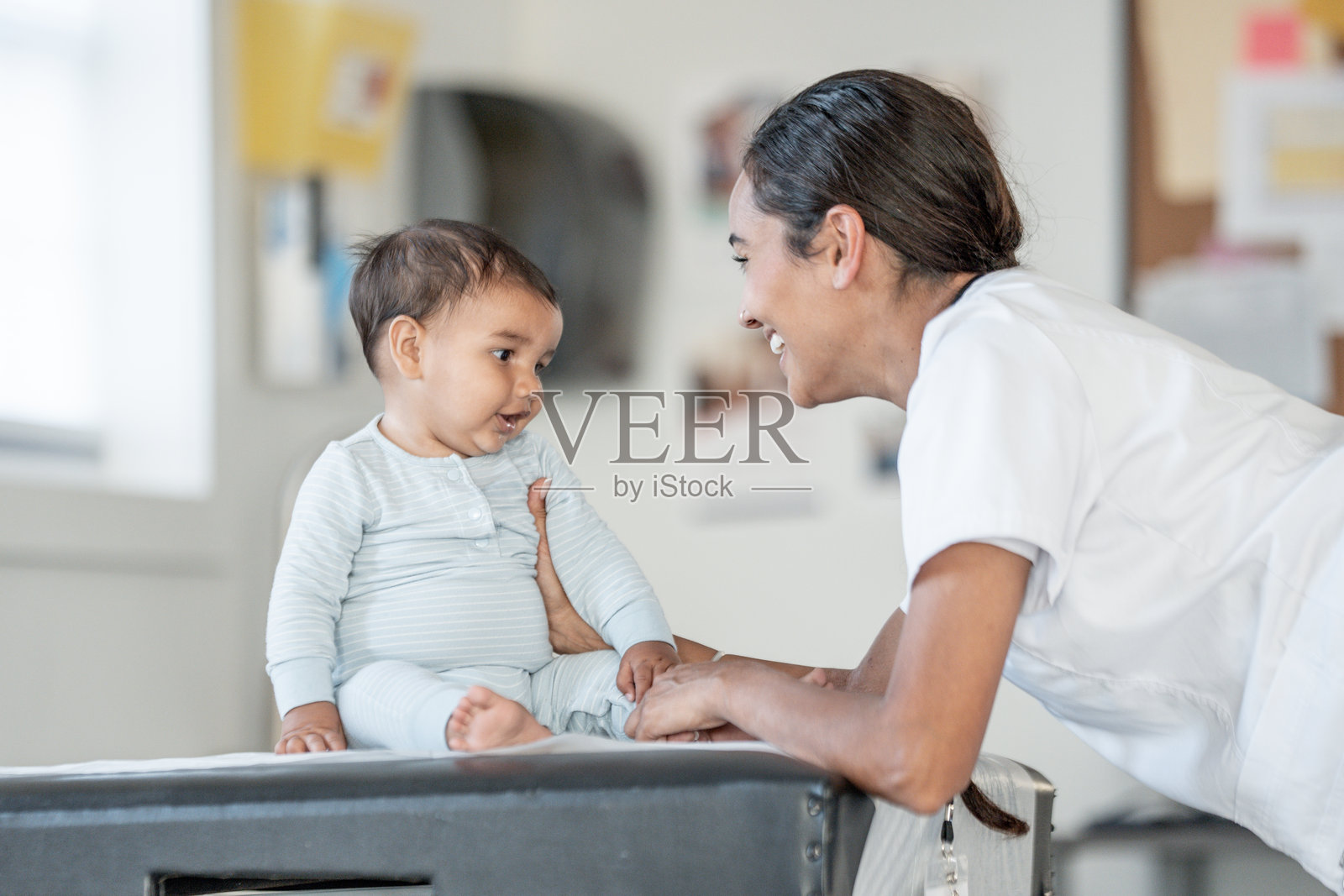 温馨的儿科检查，微笑的护士和婴儿在检查台上照片摄影图片