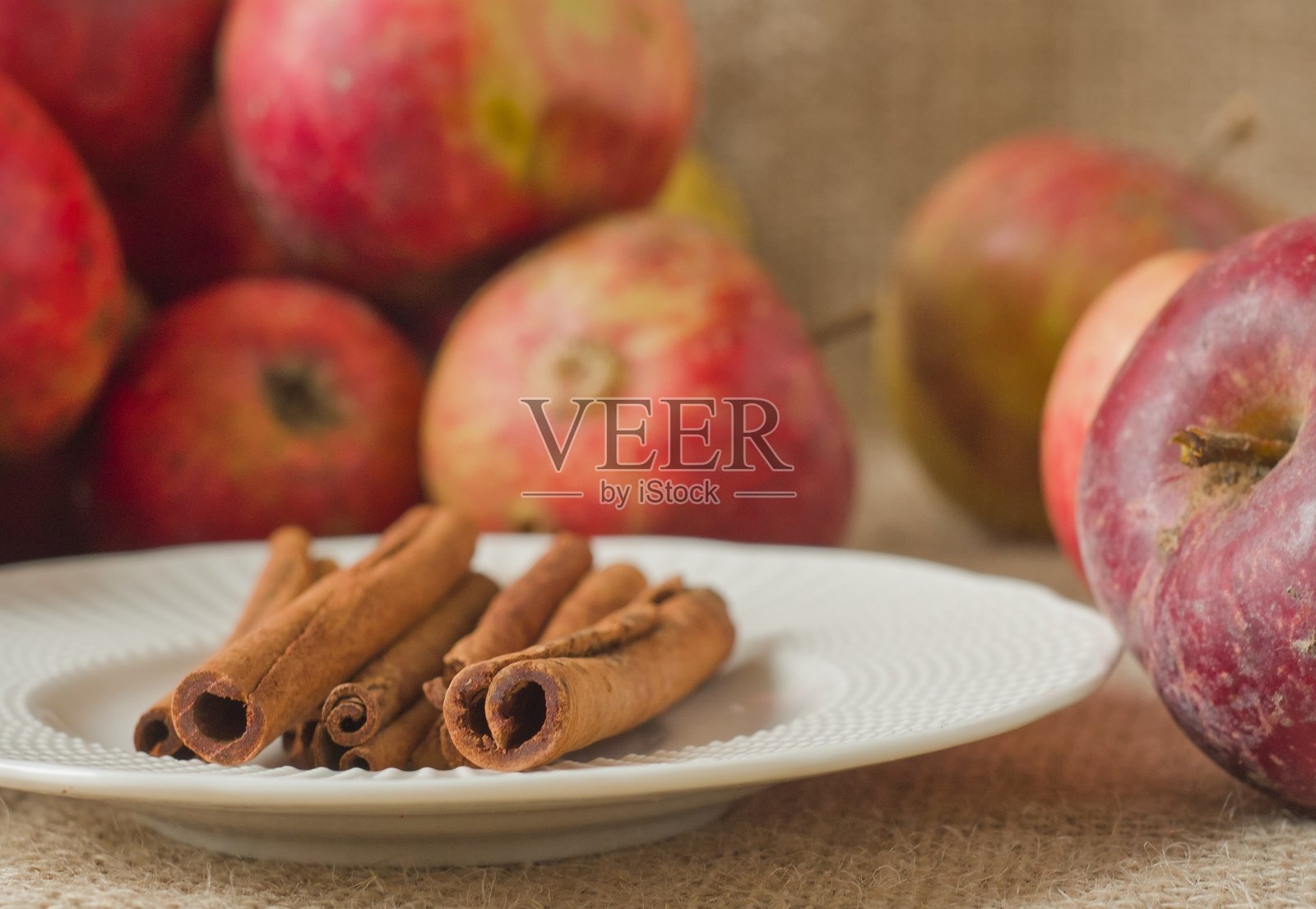肉桂和红苹果 - 几根完整的、芳香的肉桂棒堆叠在白盘上，背景是乡村粗麻布照片摄影图片