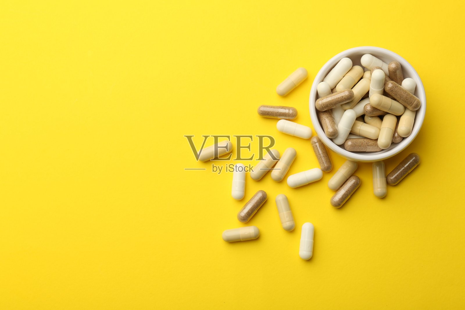 不同维生素胶囊在黄色背景上，俯视角度，留有文字空间照片摄影图片